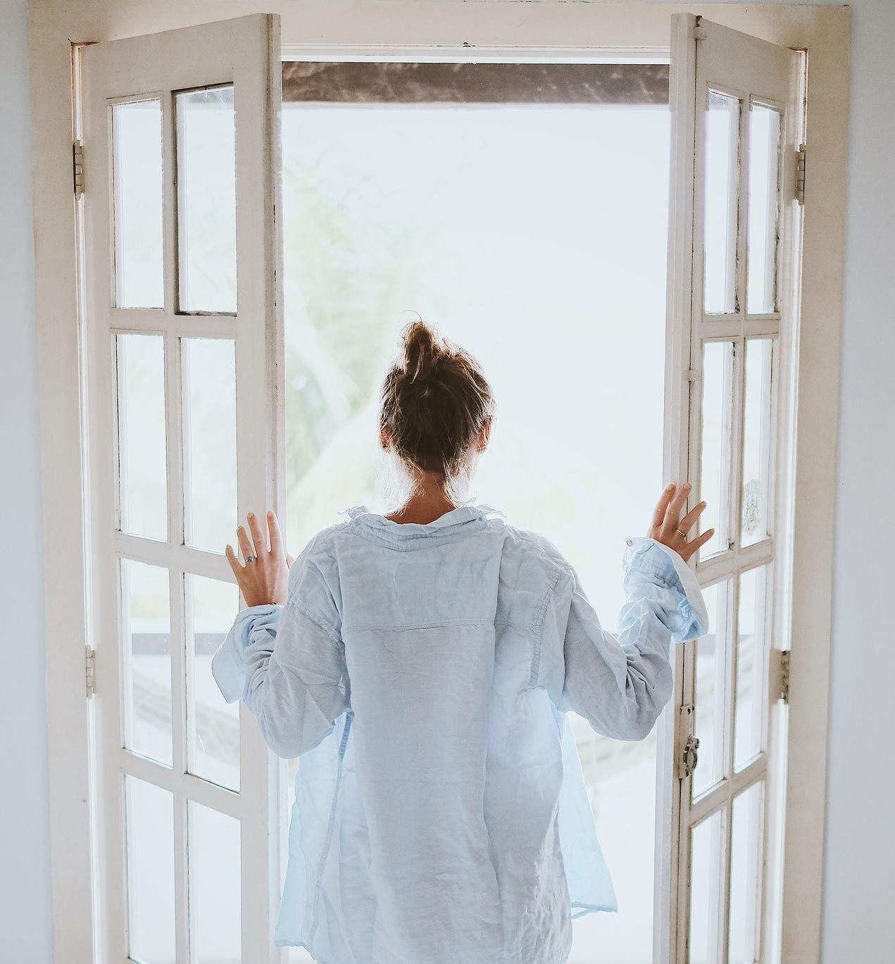 Frau an offenem Fenster, Lüften für ein gutes Raumklima und gegen Schimmelpilze
